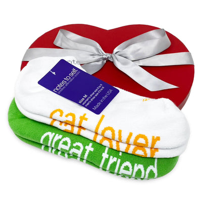 cat lover white socks with yellow words and i am a great friend green socks with white words on top of a red heart box with silver ribbon