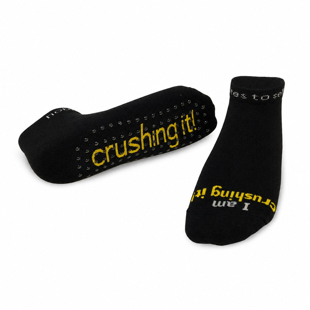 A pair of notes to self black low-cut gripper socks with yellow and grey text reading 'I am crushing it!' 