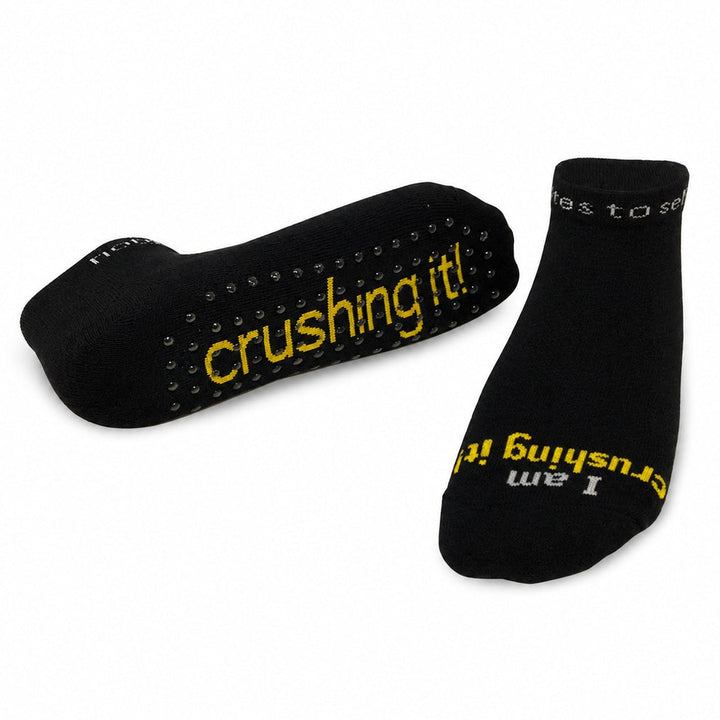 A pair of notes to self black low-cut gripper socks with yellow and grey text reading 'I am crushing it!' 